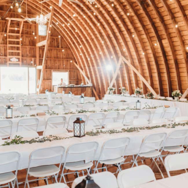A rustic barn wedding set with long tables, white chairs, and twinkling string lights.
