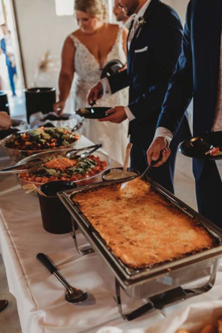 Guests in formal attire enjoy catering at a buffet table during a Minnesota wedding ceremony.