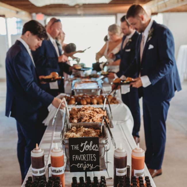 People in suits serve themselves from a buffet table at a Minnesota wedding venue event.
