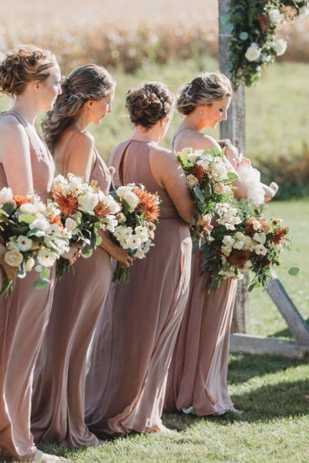 Four bridesmaids in blush dresses hold bouquets at a Rustique Barn wedding ceremony in Minnesota.