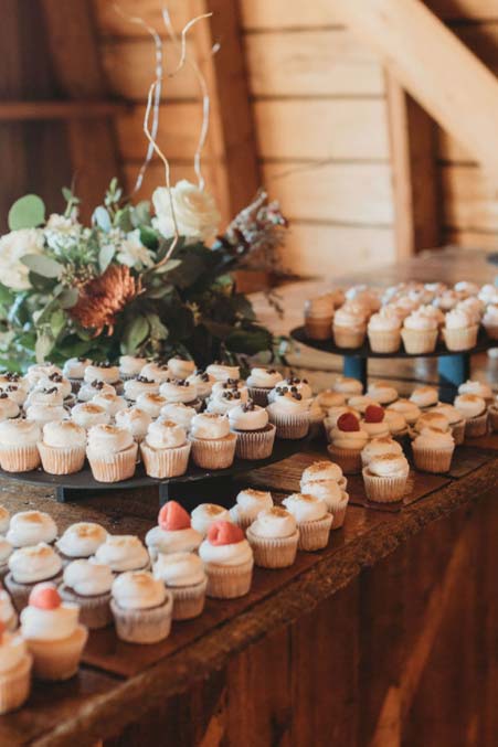 Assorted cupcakes with white frosting displayed on wooden stands at a Minnesota barn wedding.